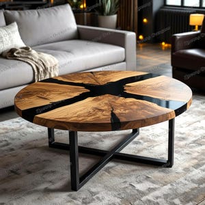 Op de afbeelding: Ronde salontafel van hout met een zwart epoxyharsontwerp. De tafel heeft een natuurlijk houtnerfpatroon met zwarte accenten en een zwart metalen onderstel. De tafel is een modern meubelstuk.