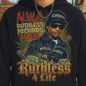 Puede incluir: Sudadera con capucha negra con un gráfico de Eazy-E, el texto "N.W.A. Ruthless Records Lives" y "Ruthless 4 Life." El diseño incluye una gorra de Compton, micrófonos, dinero y hojas de cannabis.