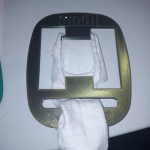 May include: A gold-coloured metal sock holder with the word "small" at the top. A white sock is hanging from the holder. The word "small" is printed on the top of the holder.