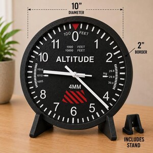 May include: A black circular wall clock designed like an aircraft altimeter with white numbers and markings. It features a 10-inch diameter, a 2-inch border, and includes a stand. The face displays the word ALTITUDE and 4MM.