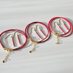 May include: Three sets of jewellery, each consisting of a red beaded bracelet and a pair of matching red beaded drop earrings. The bracelets feature gold-toned metal clasps and extender chains, while the earrings have gold-toned hook wires.