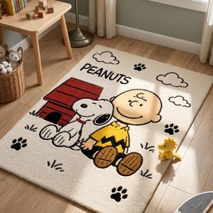 May include: A rectangular area rug featuring a cream background with a Peanuts graphic. The design includes Snoopy, Charlie Brown in a yellow shirt, a red doghouse, black paw prints, and clouds. The text PEANUTS is printed in black letters.