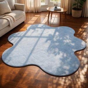 Op de afbeelding: Een lichtblauw, wolk-vormig vloerkleed. Het vloerkleed is gemaakt van een zacht materiaal en ligt op een houten vloer. De unieke vorm en kleur van het vloerkleed geven de kamer een vleugje fantasie. Het vloerkleed is een decoratief element voor een woonkamer.
