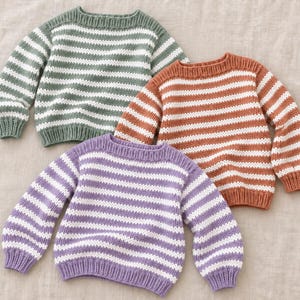 Könnte beinhalten: Drei langärmelige Strickpullover mit horizontalen Streifen in Salbeigrün, Terrakotta-Orange und Lavendel, jeweils kombiniert mit Weiß. Die Pullover haben einen Rundhalsausschnitt, gerippte Bündchen und einen gerippten Saum aus Strick.
