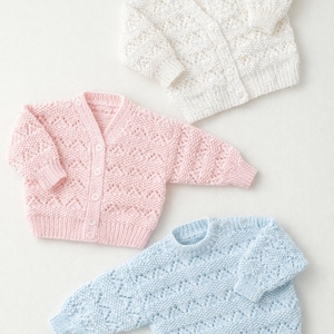 May include: Three knitted baby sweaters in soft pastel colors: white, pink, and light blue. The sweaters have a textured, open-knit design. The pink and white sweaters are cardigans with button closures, while the blue one is a pullover.
