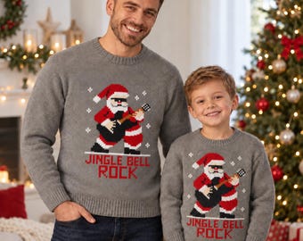 Puede incluir: Un suéter de punto gris de manga larga con un gráfico pixelado de Santa Claus tocando la guitarra eléctrica y el texto JINGLE BELL ROCK en letras rojas. El suéter presenta un cuello redondo y puños y dobladillo acanalados.