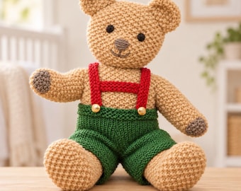 Puede incluir: Un oso de peluche tejido en color beige con almohadillas marrones oscuras, ojos negros y nariz bordada. El oso lleva pantalones cortos tejidos en verde sujetos por tirantes rojos con dos pequeños botones dorados en la cintura.