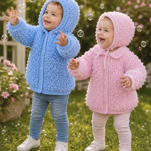 May include: Two children wearing textured knit jackets with hoods. One child wears a light blue button-up jacket with a hood over blue jeans and white trainers. The other child wears a light pink button-up jacket with a hood over pink leggings.