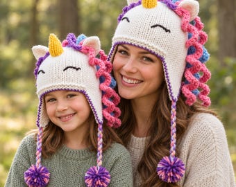 Puede incluir: Dos gorros de unicornio de punto color crema a juego con cuernos amarillos, crines de lana rizada rosa y morada, y orejeras trenzadas que terminan en pompones multicolores. Los gorros tienen ojos negros bordados y un tejido suave.