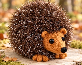 Puede incluir: Un erizo de peluche tejido a ganchillo con un cuerpo redondo cubierto de hilo marrón oscuro, brillante y puntiagudo. La cara, las orejas y los pies pequeños están hechos de hilo beige sólido, con dos ojos redondos de plástico negro y una nariz negra.