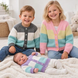 Könnte beinhalten: Drei Kinder tragen Strickjacken. Ein Kind trägt eine graue, weiße und türkisfarbene Strickjacke mit Knöpfen und blauen Jeans. Ein anderes trägt eine rosa, gelbe und türkisfarbene Strickjacke mit Knöpfen und blauen Jeans. Ein Baby trägt eine lila, weiße und türkisfarbene Strickjacke.
