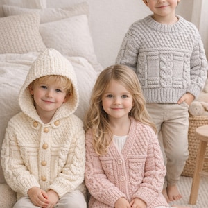 May include: Three children in knitted garments. One wears a cream hooded cardigan with wooden buttons, another a pink cardigan, and the third a grey sweater. The clothing features cable knit patterns. The children are sitting and standing.