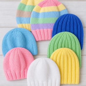 May include: A collection of eight knitted beanies in various colours. Two beanies feature horizontal pastel stripes in yellow, green, tan, blue, and pink. The other six beanies are solid colours including bright blue, light blue, pink, green, yellow, and white.