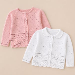 Könnte beinhalten: Zwei Baby-Strickjacken. Eine ist hellrosa, die andere ist weiß. Beide haben lange Ärmel, Knopfverschlüsse und dekorative Lochmuster am Saum und entlang der Knopfleiste. Die weiße Strickjacke hat einen Bubikragen.