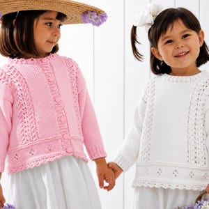 May include: A light pink button-down knit cardigan and a white knit pullover jumper, both featuring long sleeves, a round neckline, and a textured pattern with vertical cable-knit panels and a decorative openwork border along the bottom hem.