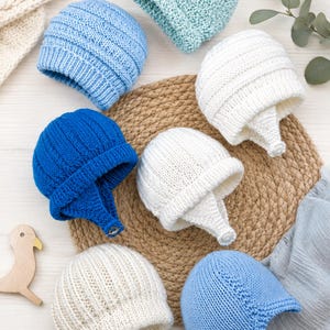 May include: A collection of seven knitted hats in various colours including light blue, bright blue, white, and mint green. Each hat features a ribbed texture, a folded brim, and a small chin strap with a button closure for a secure fit.