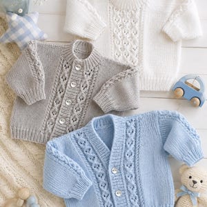 May include: Three long-sleeved knit sweaters in white, light gray, and light blue. Each sweater features a central vertical cable knit pattern, ribbed cuffs and hems, and a button-front closure. The white sweater has buttons on the shoulder.