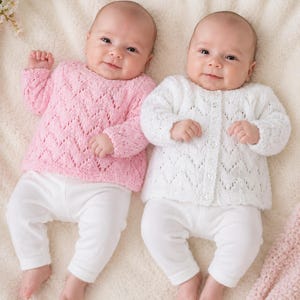 Può includere: Due neonati indossano maglioni in maglia a maniche lunghe con un motivo a pizzo chevron. Un maglione è rosa chiaro e l'altro è bianco con un'apertura frontale a bottoni. Entrambi i neonati indossano leggings bianchi semplici su una superficie morbida.