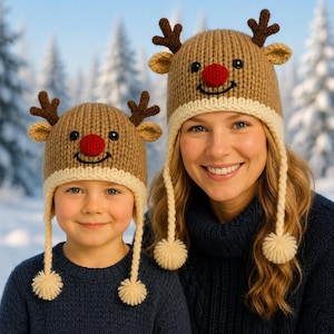 Könnte beinhalten: Zwei passende beige Strickmützen mit roter Bommelnase, schwarzen Knopfaugen, aufgesticktem Lächeln und braunem Geweih. Jede Mütze hat einen cremefarbenen Rippsaum und zwei lange geflochtene Ohrenklappen, die in cremefarbenen Garnbommeln enden.