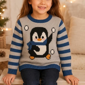 Peut inclure: Un pull à manches longues gris avec un motif central représentant un pingouin noir et blanc portant une écharpe bleue. Le pull présente un col rond bleu, des poignets et un ourlet côtelés bleus, ainsi que des rayures grises et bleues.