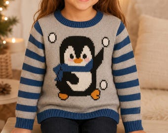 Puede incluir: Un suéter gris de manga larga con un gráfico central de un pingüino blanco y negro que lleva una bufanda azul. El suéter tiene un cuello redondo azul, puños y dobladillo acanalados en azul, y mangas con rayas horizontales grises y azules.