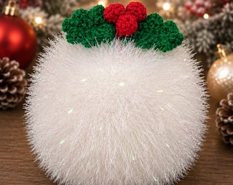 May include: A spherical, white, fuzzy, textured ornament featuring a crocheted holly decoration on top. The holly consists of three small, round, red berries and two green, jagged-edged leaves, all crafted from yarn.
