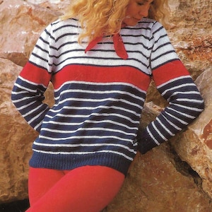Puede incluir: Un suéter a rayas con rayas horizontales azul marino, blancas y rojas. El suéter tiene mangas largas y una corbata roja. La persona de la imagen lleva leggings rojos. El fondo es una superficie rocosa.