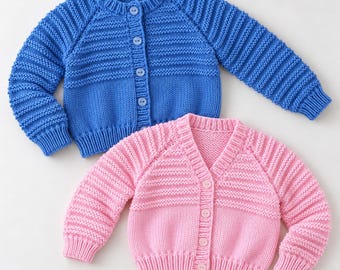 Puede incluir: Un cárdigan de punto azul brillante de manga larga con cuello redondo y cuatro botones, colocado sobre un cárdigan de punto rosa claro de manga larga con cuello en V y cuatro botones. Ambas prendas tienen mangas acanaladas y cuerpo liso.