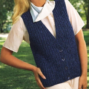 May include: A navy blue knitted vest with a V-neck and button closure. The vest is worn over a light pink short-sleeved shirt and a white collared shirt. The image is taken outdoors with a green background.