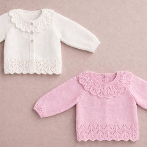 May include: Two baby sweaters, one white and one pink, with scalloped collars and hems. The white sweater is a button-up cardigan. The pink sweater is a pullover. Both have long sleeves and are made of a soft knit material.