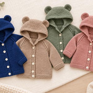 May include: Four knitted cardigans with hoods featuring small bear ears. The sweaters are in navy blue, beige, olive green, and dusty rose. Each long-sleeved garment has a front button closure with light-colored circular buttons and ribbed cuffs.