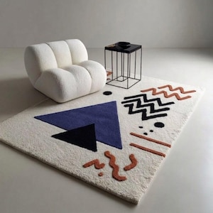 May include: A cream-colored geometric rug with a blue triangle, black triangle, and brown zig-zag and line designs. A white, rounded armchair and a black side table with a black top and thin black legs are also in the image.