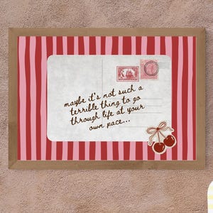 May include: A framed print with a red and pink striped background and a white rectangle with text that reads "maybe it's not such a terrible thing to go through life at your own pace...". A yellow and white striped vase and flowers are on a table.