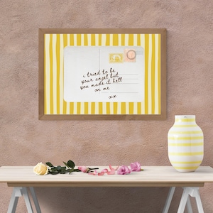 May include: A framed print with a yellow and white striped background and a postcard design. The postcard has handwritten text that reads "I tried to be your angel but you made it hell on me." A white and yellow striped vase and flowers are on a table.
