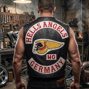 Könnte beinhalten: Schwarze Lederweste mit Aufnähern "HELLS ANGELS" und "GERMANY" in Rot und Weiß. Die Weste zeigt ein Totenkopf-mit-Flügeln-Emblem. Das Bild ist in einer Werkstatt mit Werkzeugen und einem Motorrad im Hintergrund aufgenommen.