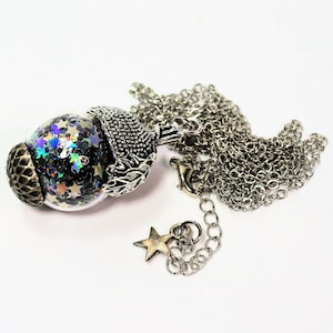 May include: A silver acorn pendant necklace with a clear glass orb filled with iridescent glitter stars. The necklace has a silver chain with a star charm.