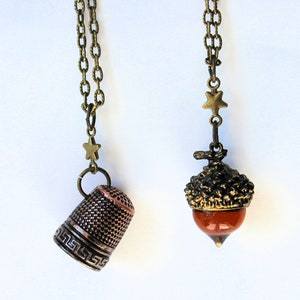 Op de afbeelding: Twee kettingen met bronzen kettingen en sterbedels. De ene ketting heeft een koperen vingerhoedbedel, de andere heeft een bruine eikelbedel.