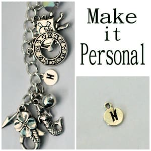 May include: A silver charm bracelet with a variety of charms, including a clock, a mermaid, a flower, a lightning bolt, and a letter H charm. The bracelet is on a white background. Make it Personal.
