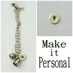 May include: A silver charm bracelet with a thimble, a globe, and a charm with the letter "P" on it. The bracelet has a silver clasp and a silver chain. The charms are all silver and have a vintage look. The text "Make it Personal" is written below the bracelet.