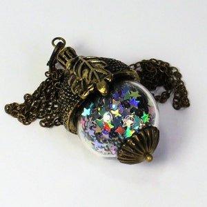 May include: A gold acorn pendant necklace with a clear glass orb filled with iridescent star-shaped glitter. The pendant is attached to a gold chain.