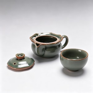 May include: A green ceramic tea set comprising a teapot, lid, and teacup. The teapot features a handle and spout, and the lid has a small knob. The teacup is round. The set has a brown rim.