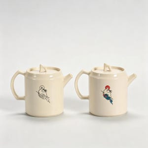 Peut inclure: Deux théières crème avec une anse, un bec et un couvercle. Chaque théière présente une illustration différente d'un oiseau. Un oiseau est noir, l'autre est rouge, bleu et blanc. Les théières sont sur fond blanc.