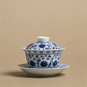 Könnte beinhalten: Ein weißes Porzellan-Teeservice mit blauen Blumenmustern. Das Set besteht aus einer Schale mit Deckel, einer Untertasse und einem kleinen, runden Deckel. Das blau-weiße Design ist aufwendig und bedeckt die gesamte Oberfläche der Teile.