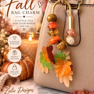 May include: A gold-toned metal bag charm featuring a U-shaped clasp adorned with various beads in shades of brown, orange, and pink, accented with multiple translucent acrylic leaf-shaped charms in autumn colors of orange, red, green, and cream.