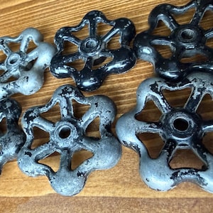 Könnte beinhalten: Eine Sammlung von Vintage-Wasserhahn-Griffen. Die Griffe sind aus Metall und haben ein sternförmiges Design mit fünf Spitzen. Einige sind schwarz lackiert, andere silbern mit abblätternder schwarzer Farbe, was ihnen ein rustikales Aussehen verleiht.