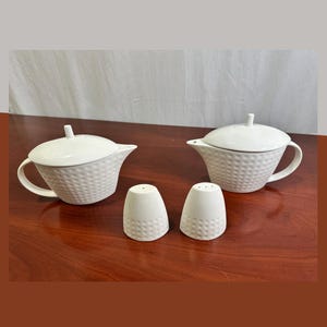 May include: A white ceramic set consisting of two lidded teapots and two matching shakers. Each piece features a textured, dimpled surface pattern. The teapots have curved handles and lids with small knobs, while the shakers are conical in shape.