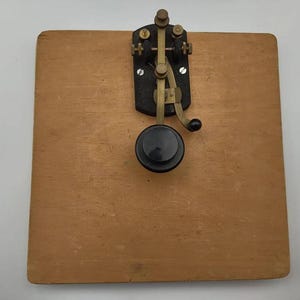 May include: A white ceramic mug with a black handle and the text "But First, Coffee" in a black, bold font. The mug is sitting on a wooden surface. The mug is approximately 4 inches tall.