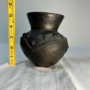 May include: A dark brown, handcrafted pottery vase with a rounded body and a flared rim. The vase features textured patterns, including raised dots and a chevron design. The height of the vase is approximately 5 inches.