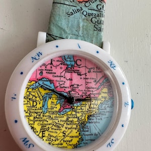 May include: A white ceramic mug with a black handle and the text "But First, Coffee" in a black, handwritten-style font. The mug is on a white surface.