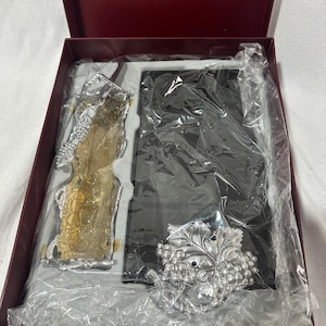 May include: A boxed set featuring a silver-toned picture frame and decorative wine-themed accessories. The frame is black, and the accessories include a grape cluster and a wine bottle-shaped item. The box is burgundy.